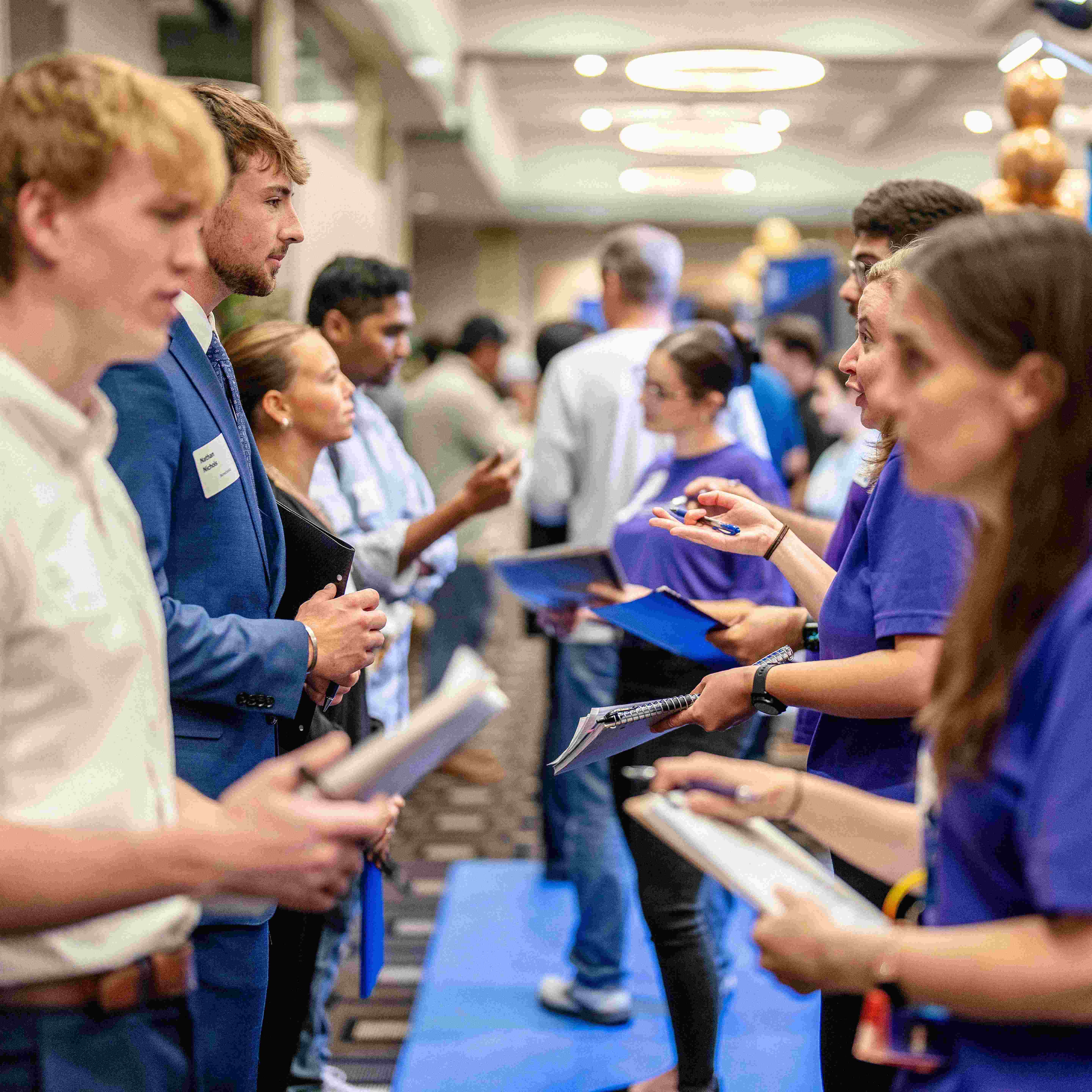 Students at the 2024 Fall Career & Internship Fair hold resumes and pads while talking to recruiters