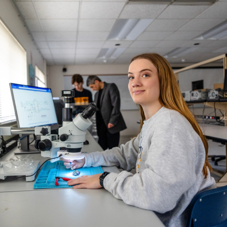 student working in embedded sytems lab with student and faculty in background