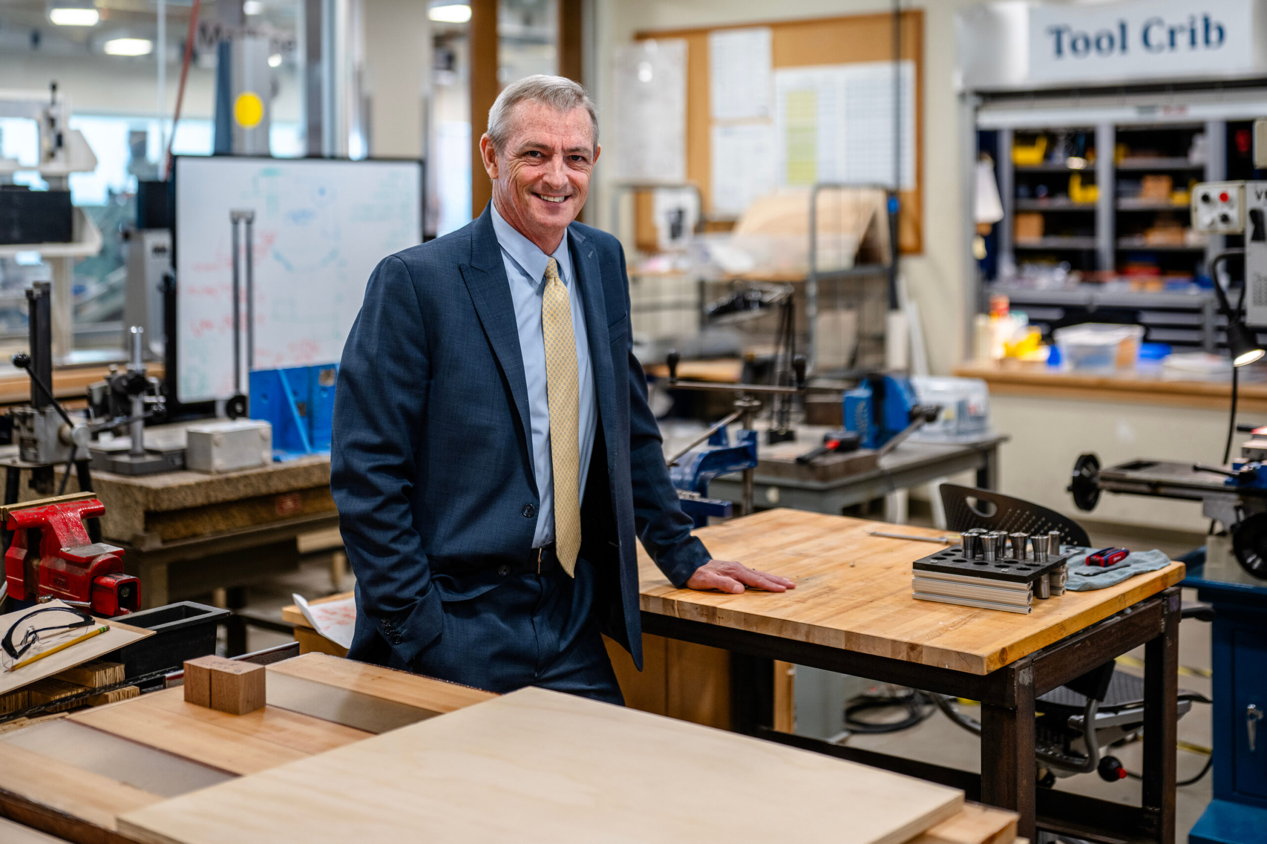 Potrait of President Lovell standing in a woodshop surrounded by tools.