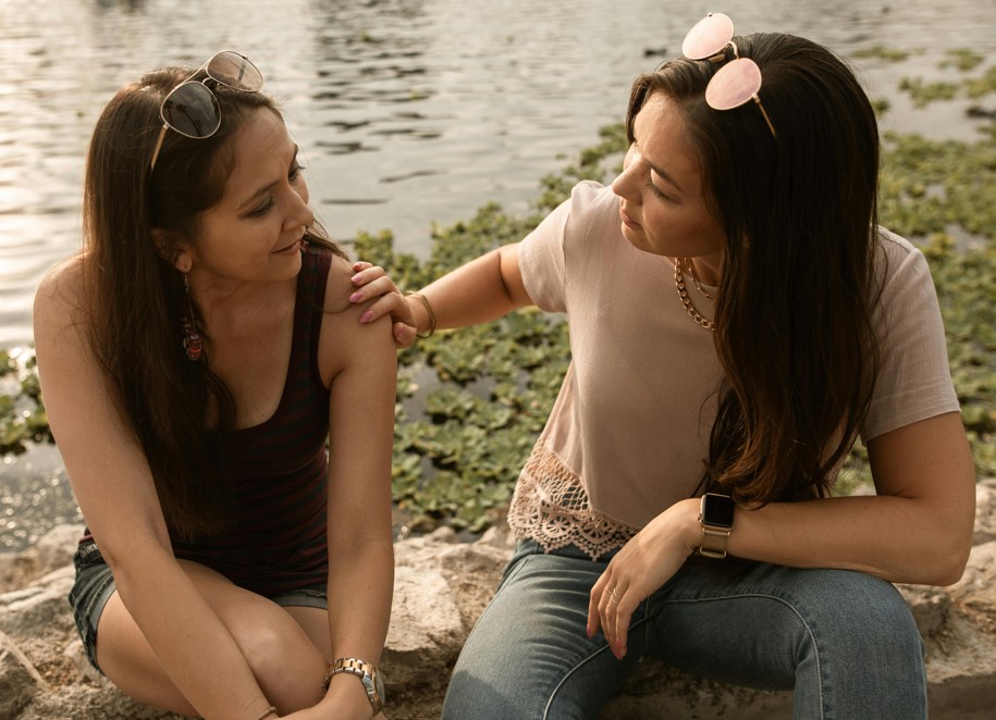 two female adults sitting outside talking in front of a body of water