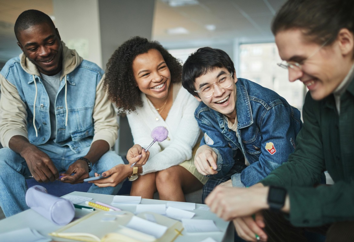 four young adults sitting around a table laughing